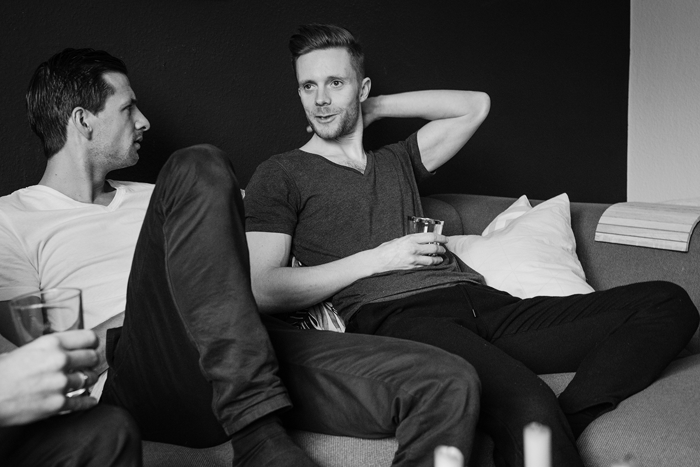 Schwarzweißfoto: Bräutigam entspannt mit einem Freund bei Drinks auf dem Sofa