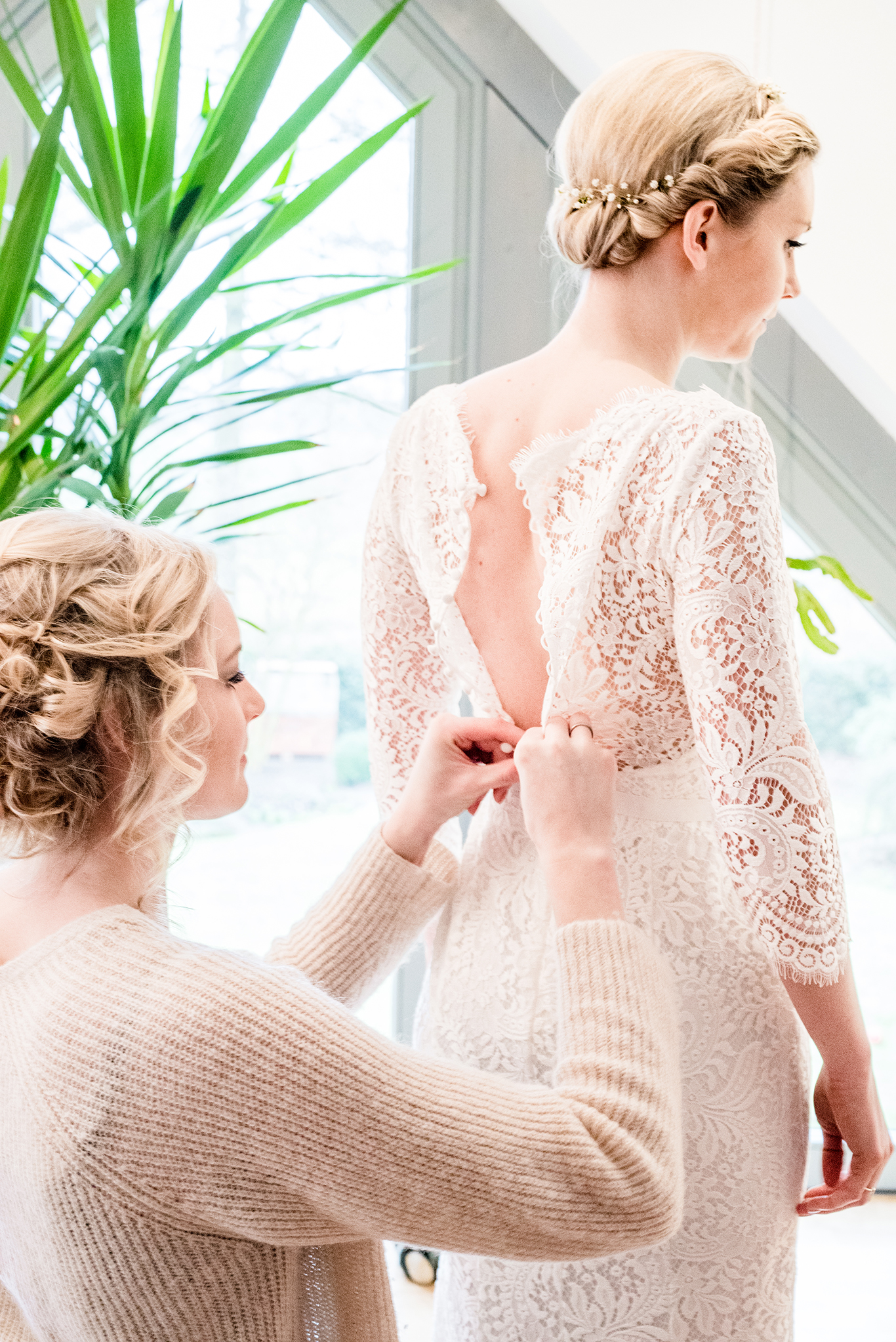 Braut wird vor dem Fenster in ihr Spitzenkleid geknöpft