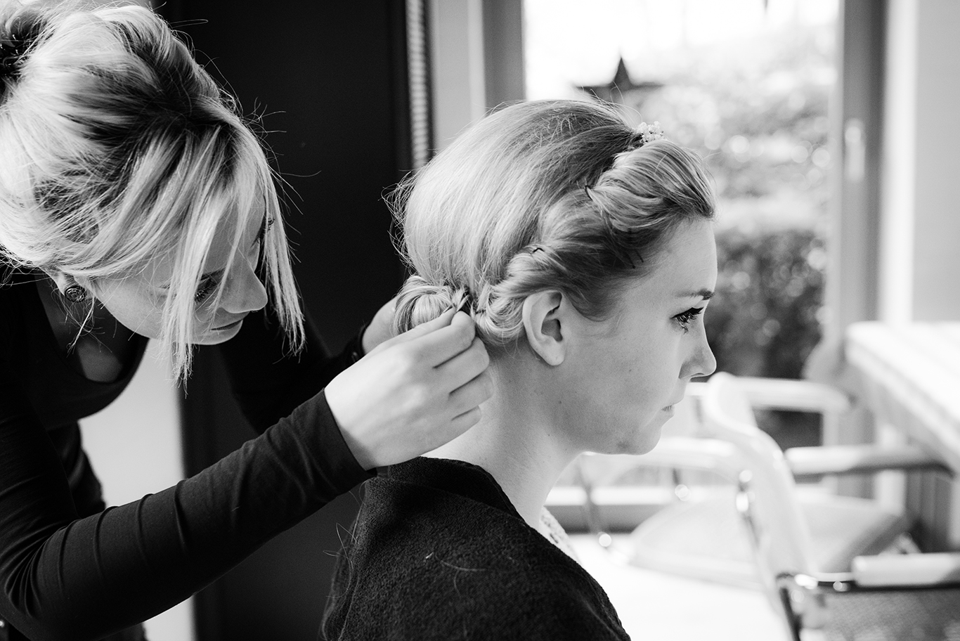 Schwarzweißfoto: Friseurin flicht der Braut die Haare vor der Trauung
