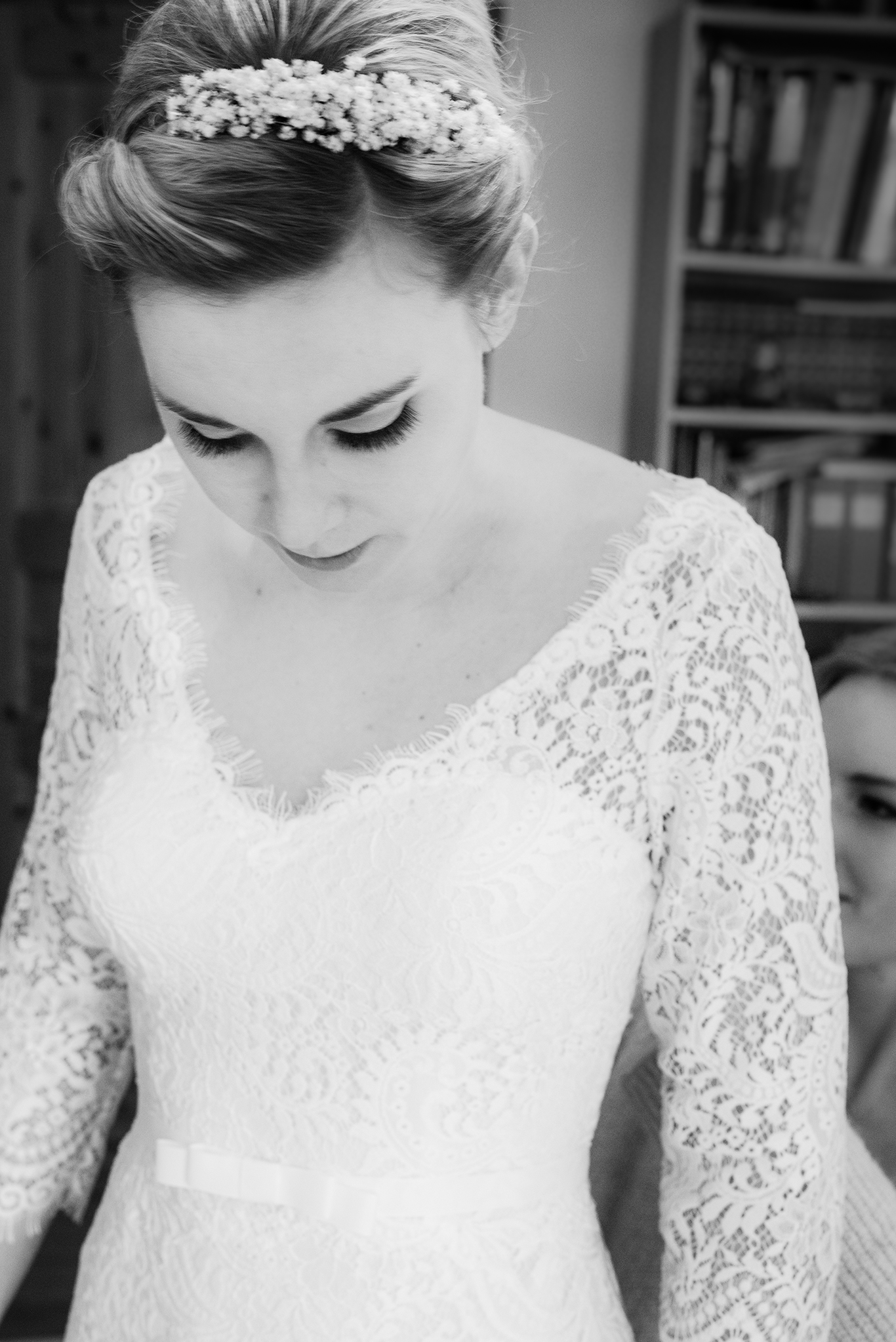 Schwarzweißfoto: Braut im Spitzenkleid mit Perlen-Haarschmuck blickt nach unten