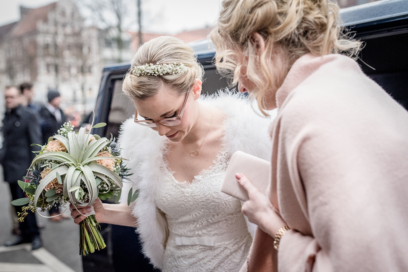 Braut mit Pelzstola steigt aus dem Hochzeitsauto, Freundinnen helfen ihr in Lüneburg