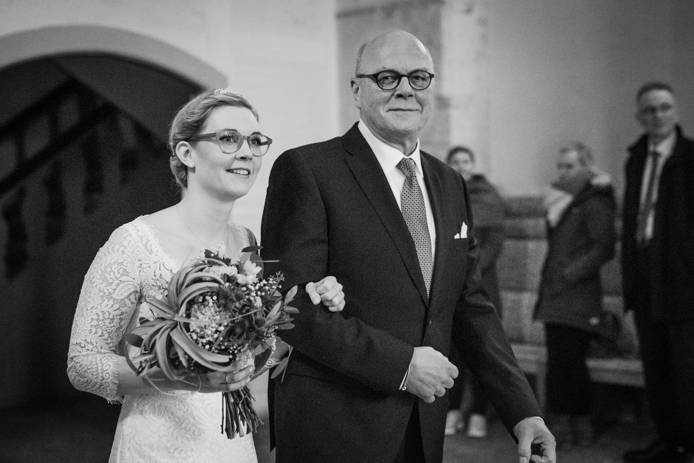 Vater führt die Braut mit Blumenstrauß zur Trauung