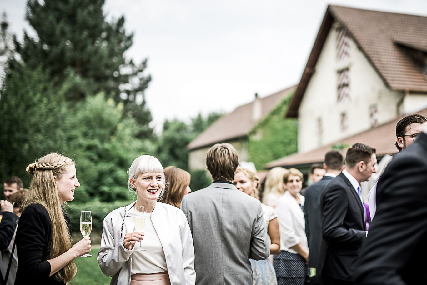 Gäste stehen mit Sektgläsern beisammen vor einem Fachwerkhaus