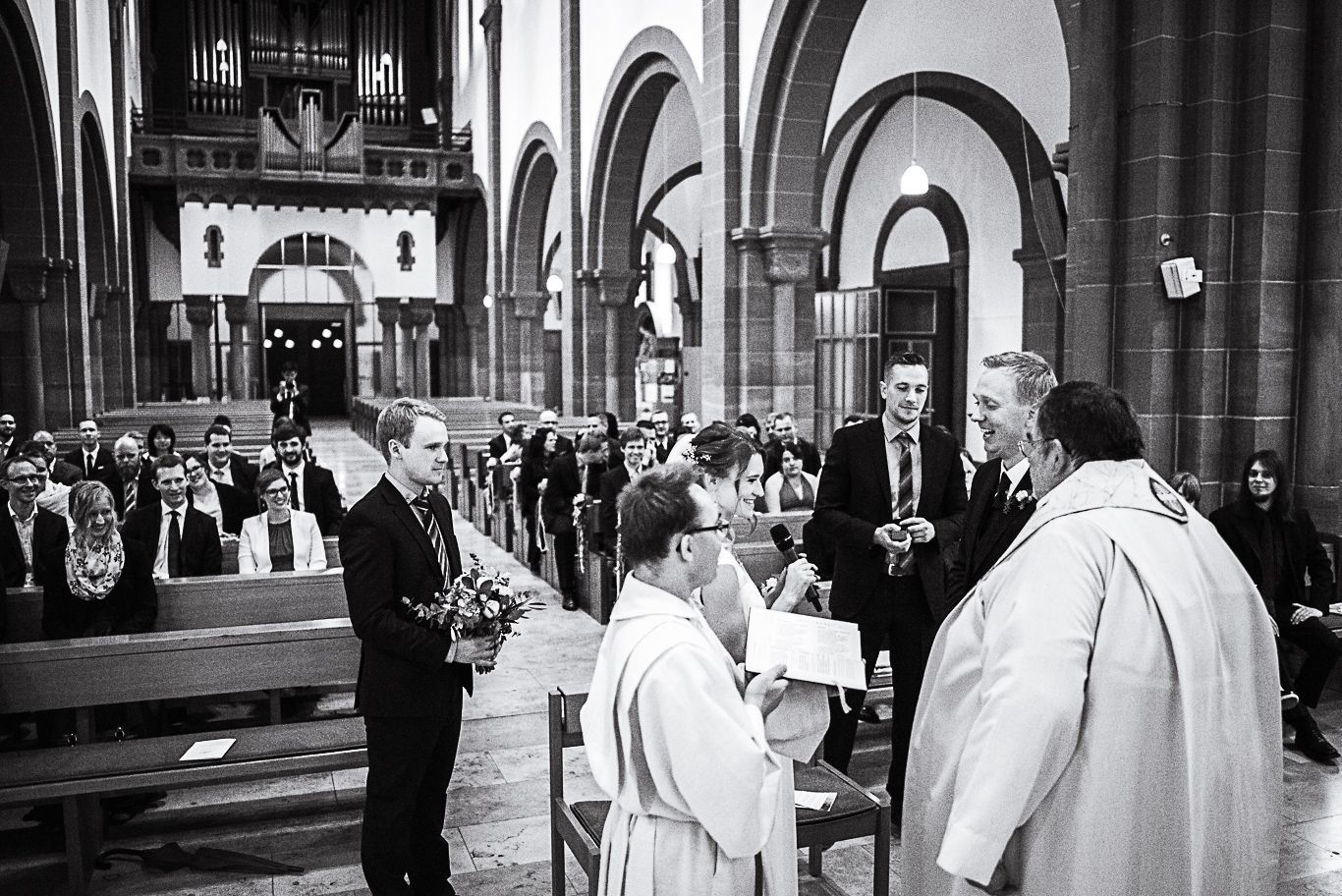 Priester begrüßt das Brautpaar am Altar von hinten fotografiert