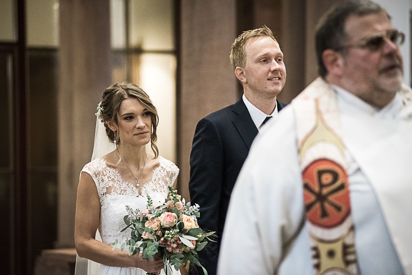 Bräutigam und Braut stehen neben dem Priester in der Kirche