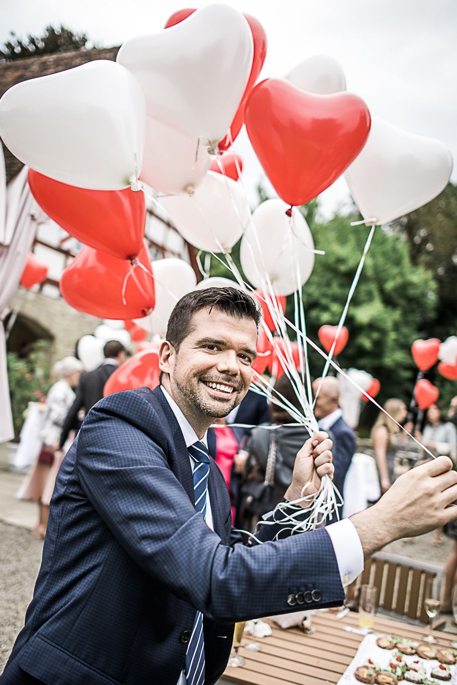 Bräutigam hält ein Bündel herzförmiger Luftballons in den Händen