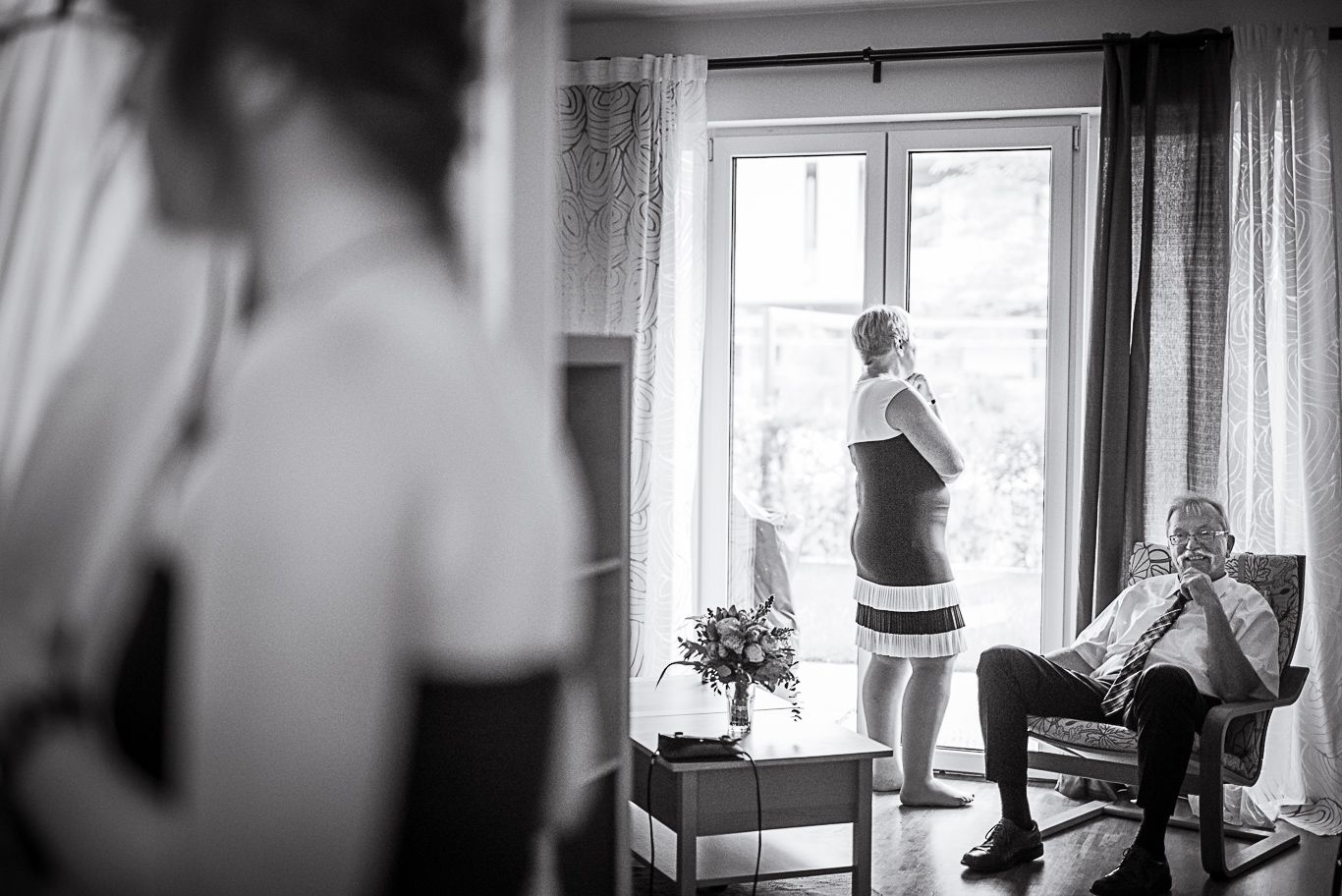 Braut steht am Fenster, Vater sitzt im Sessel, Schwarzweißaufnahme