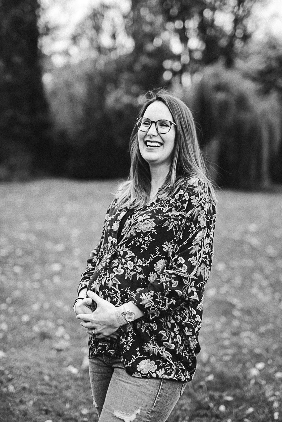 Schwangere Frau steht lächelnd im Park und hält ihren Bauch