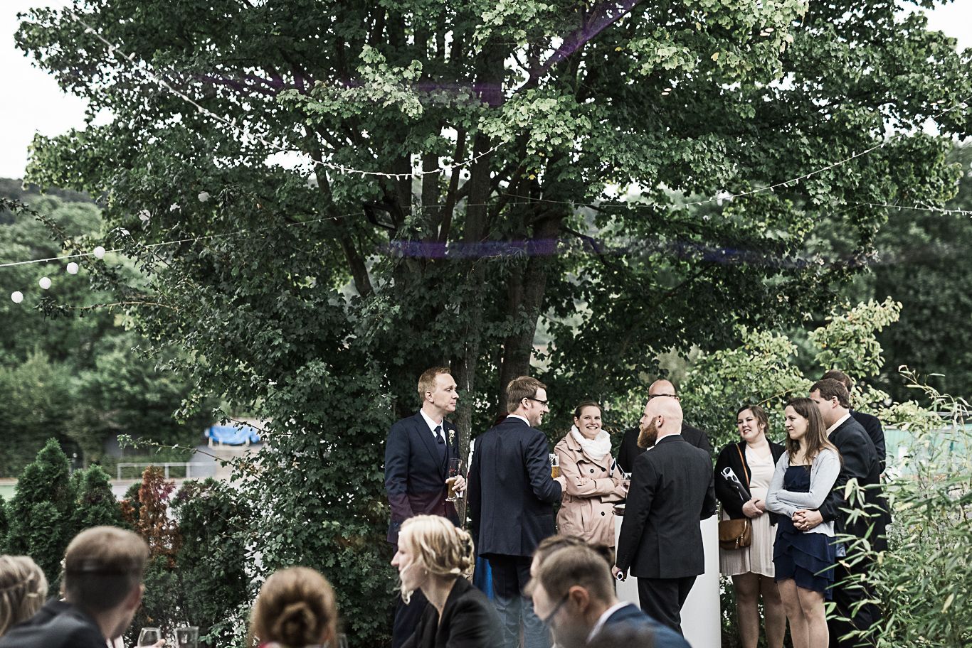 Gäste unterhalten sich stehend unter Lichterketten im Garten
