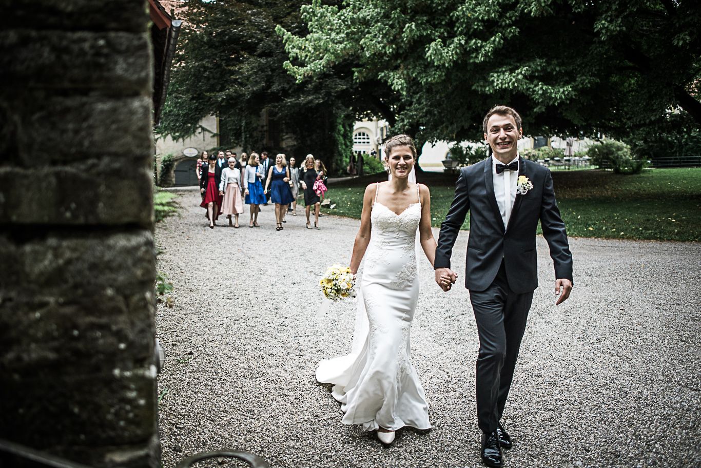 Brautpaar geht lächelnd über den Kiesweg im Schlosshof