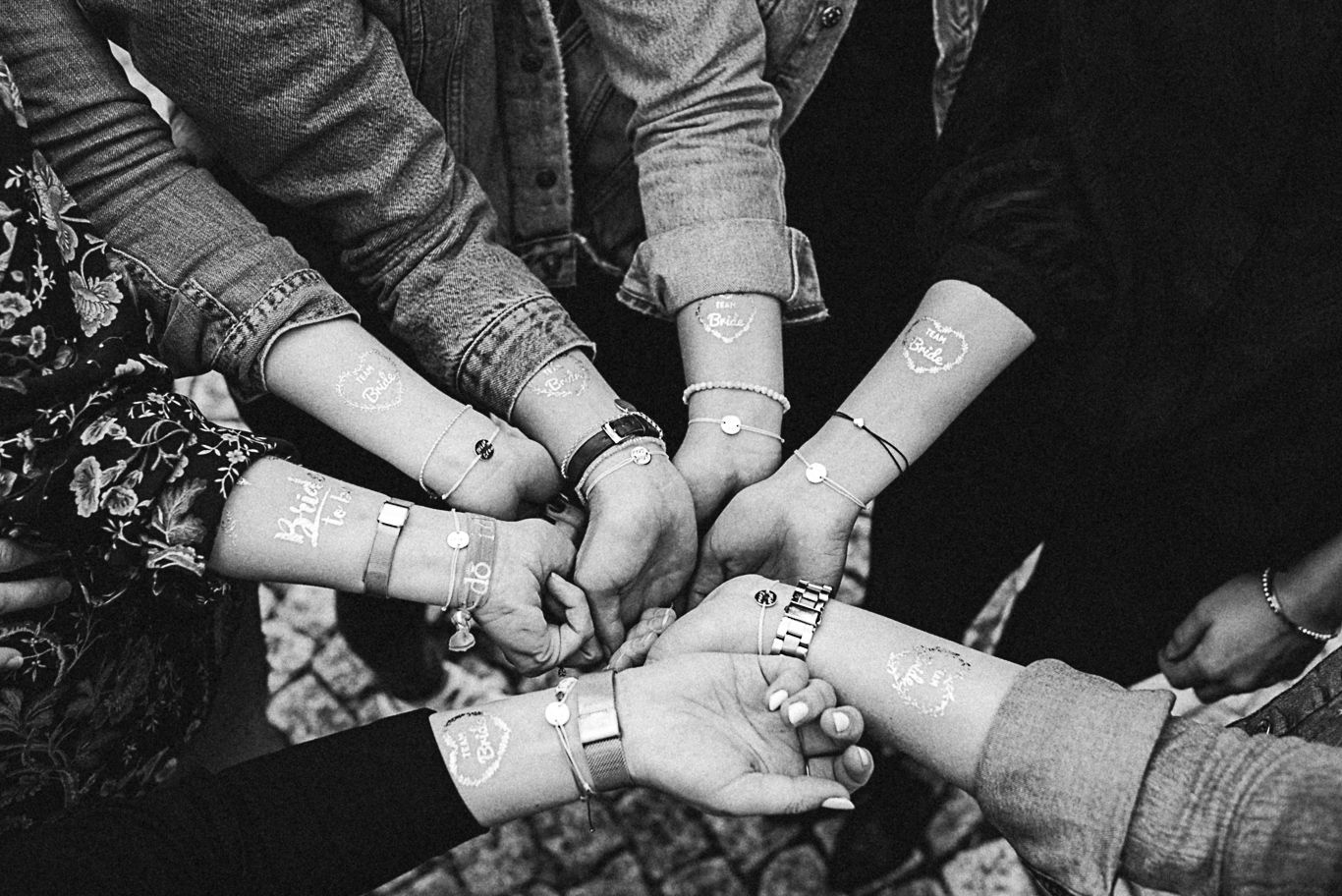 Gruppe hält verschränkte Handgelenke mit Armbändchen zusammen, Schwarzweißaufnahme