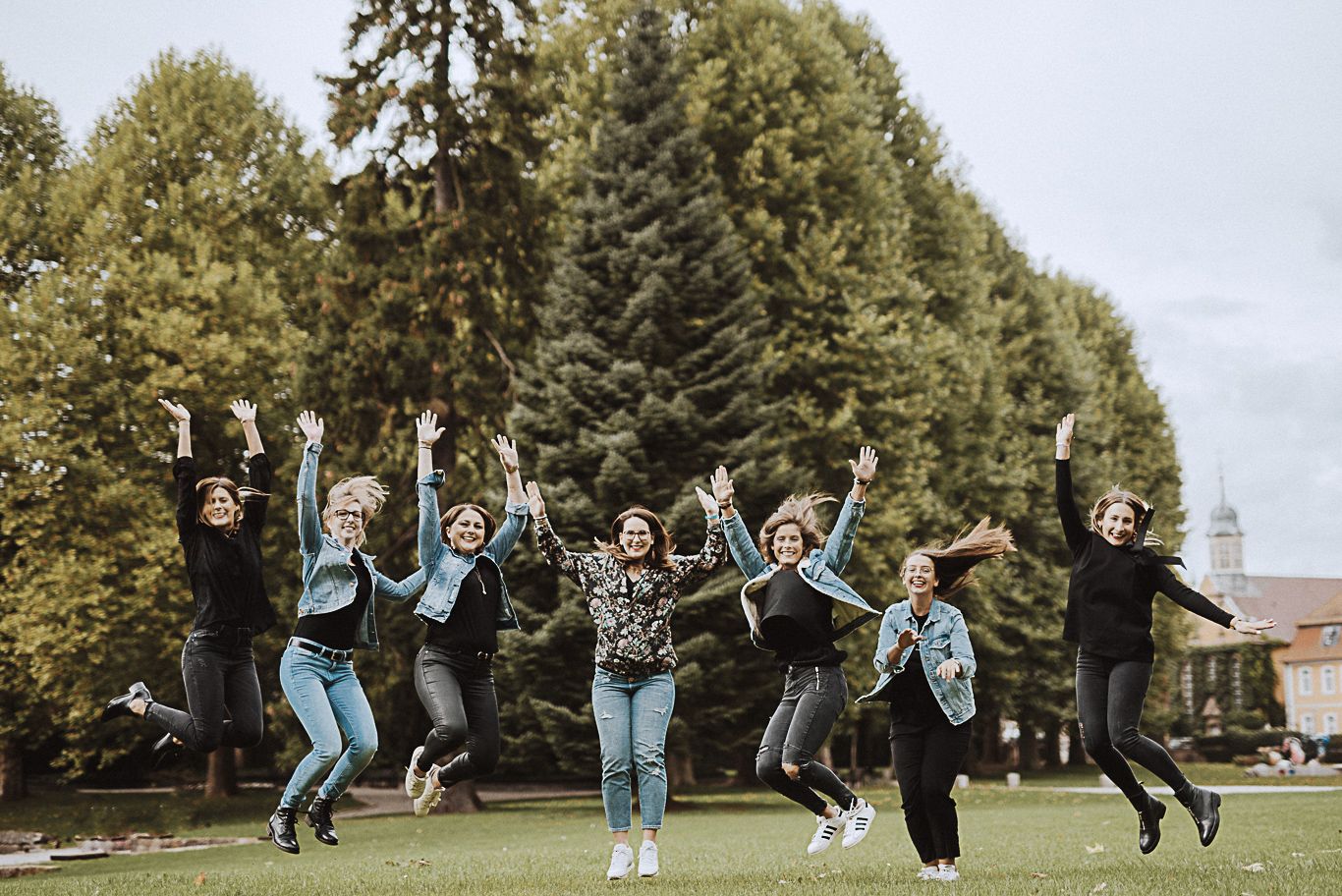 Frauengruppe jubelt springend vor Bäumen im Park