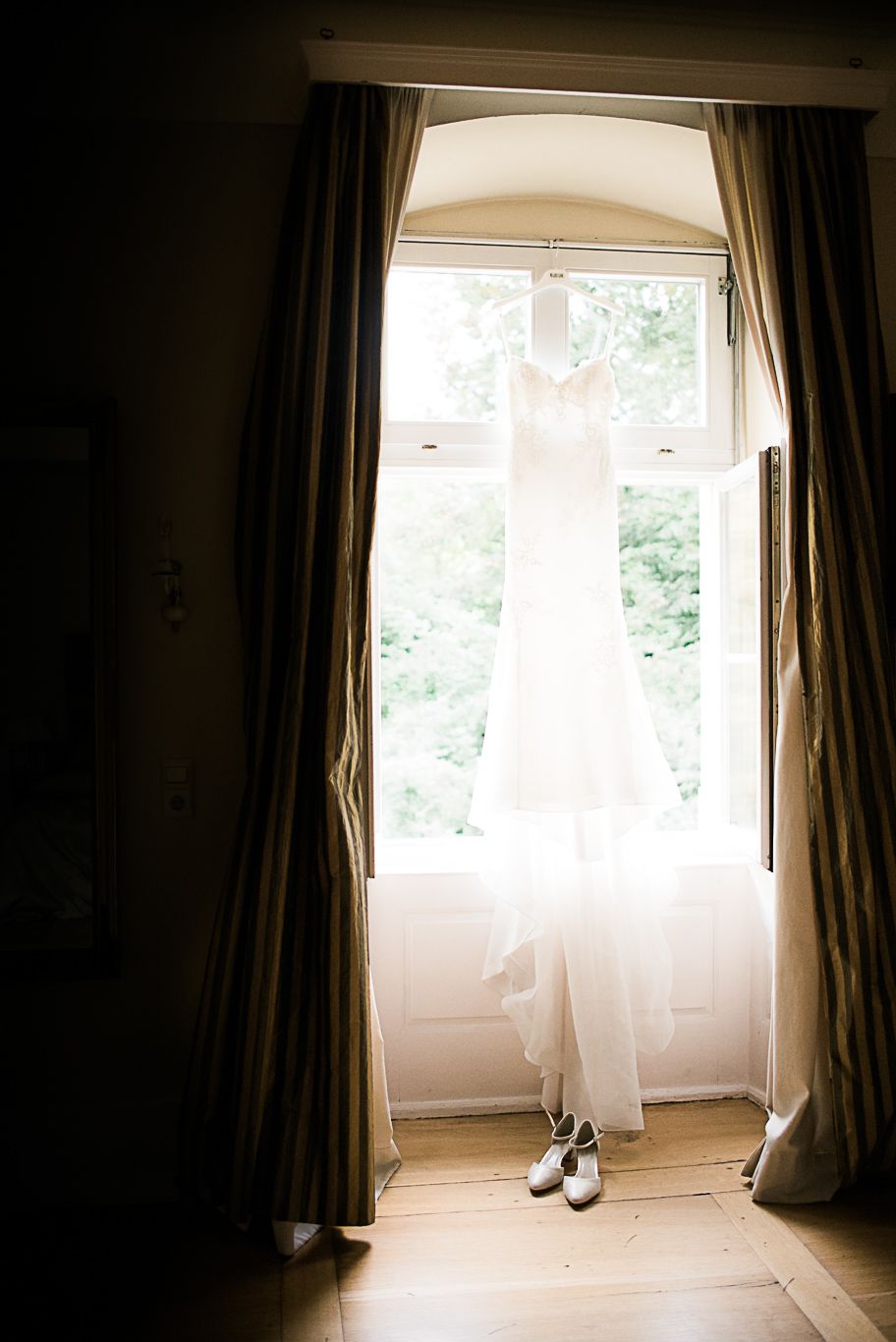 Brautkleid hängt im offenen Fenster eines Schlosszimmers