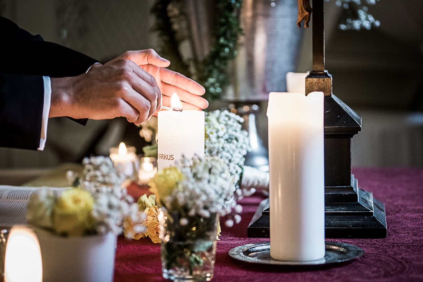 Hand entzündet eine weiße Kerze mit Blumendekoration auf dem Altar