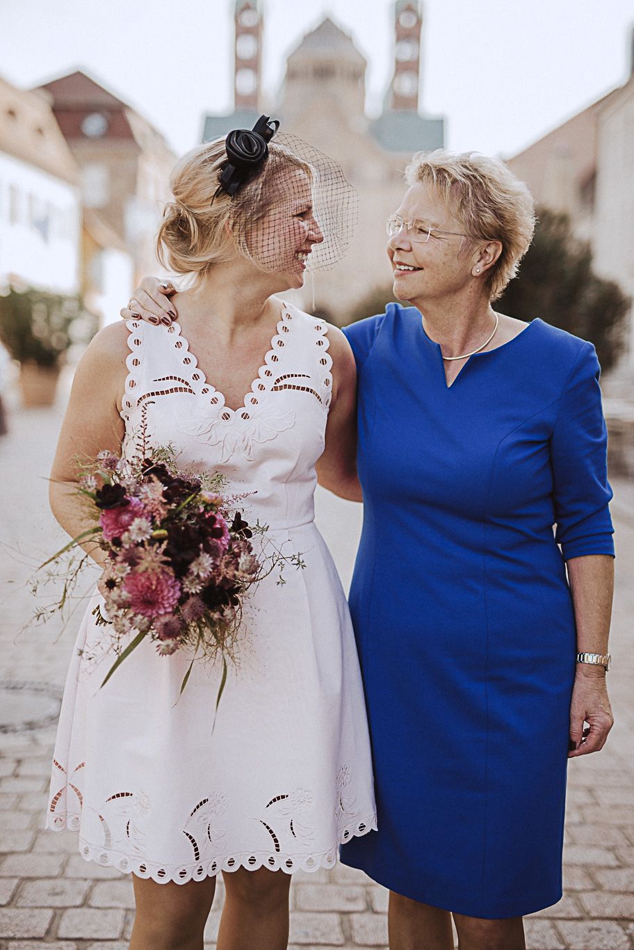 Braut mit Blumenstrauß lächelt ihre Mutter im blauen Kleid an