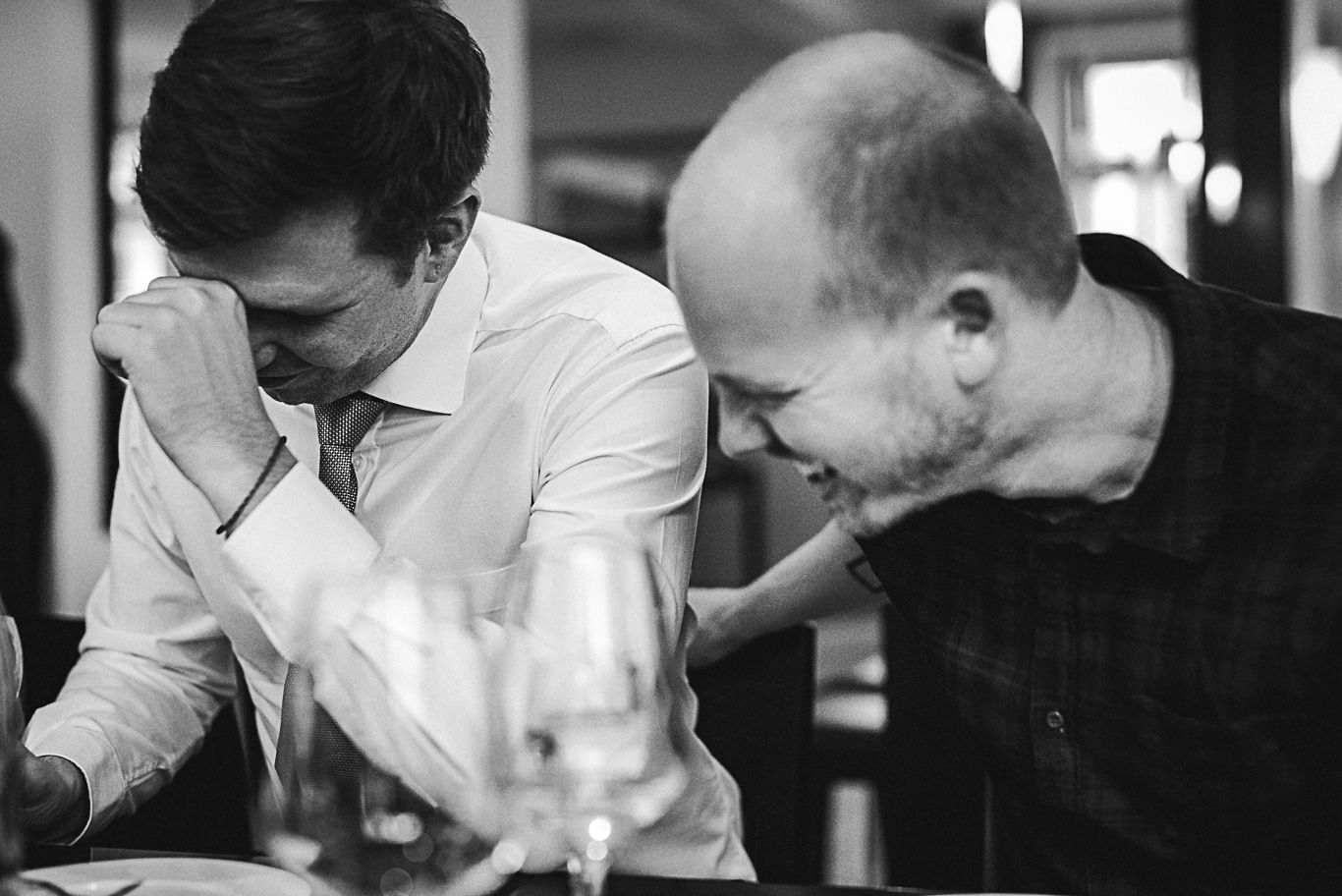 Schwarzweißaufnahme, zwei Männer lachen gebeugt über ein Geschenk