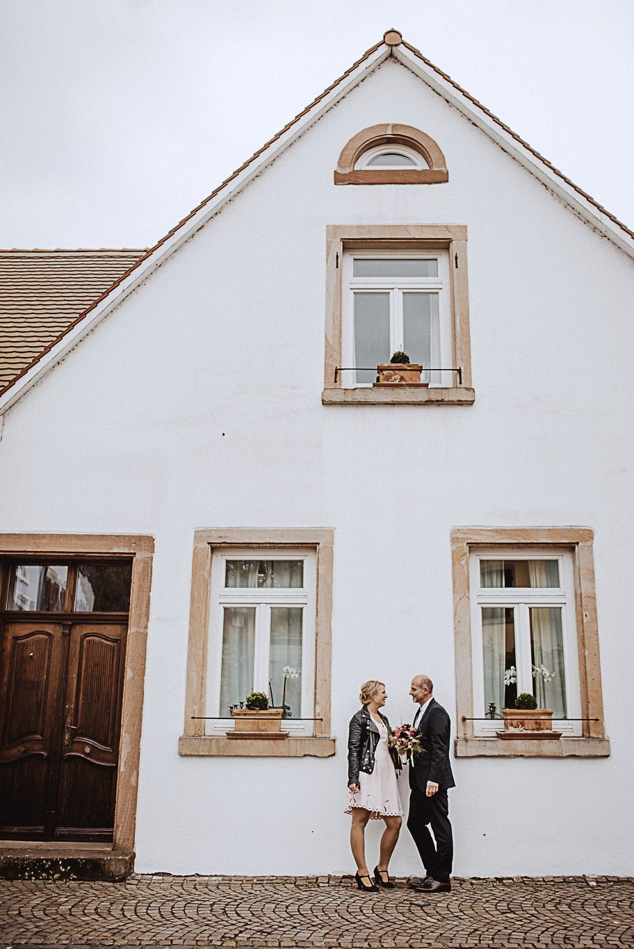 Brautpaar steht Hand in Hand vor einem weißen Giebelhaus