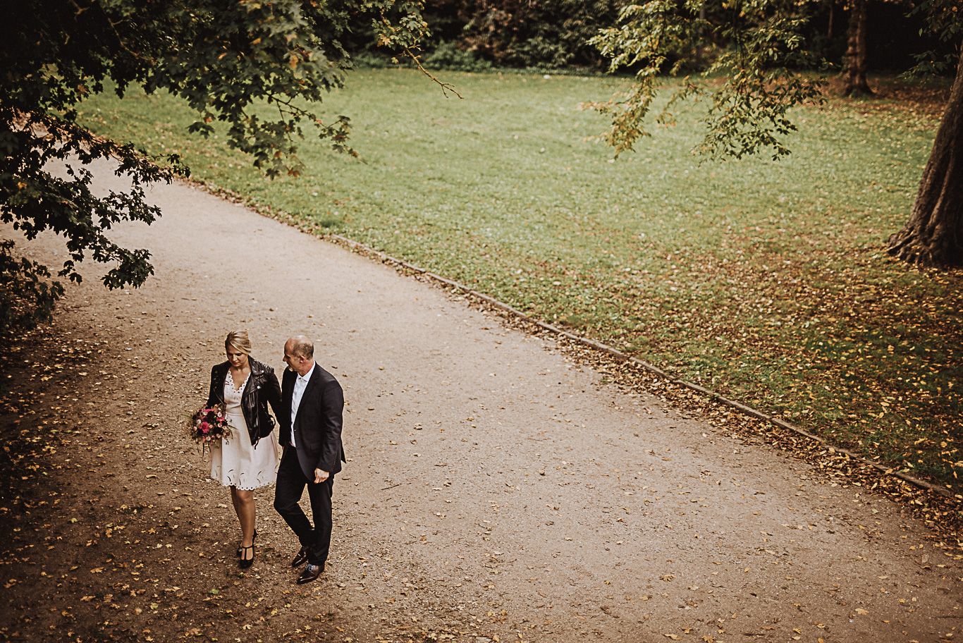 Brautpaar geht Hand in Hand einen Kiesweg im Park entlang