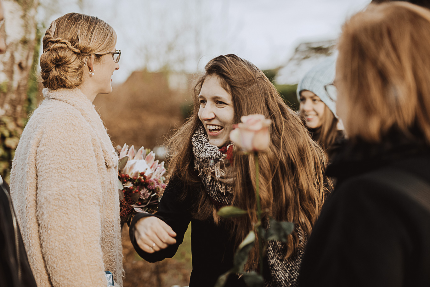 Frau überreicht lächelnd Blumen an eine Freundin im Winter