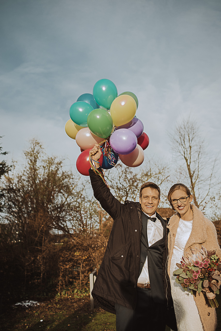 Brautpaar lacht mit bunten Luftballons auf der Winterwiese