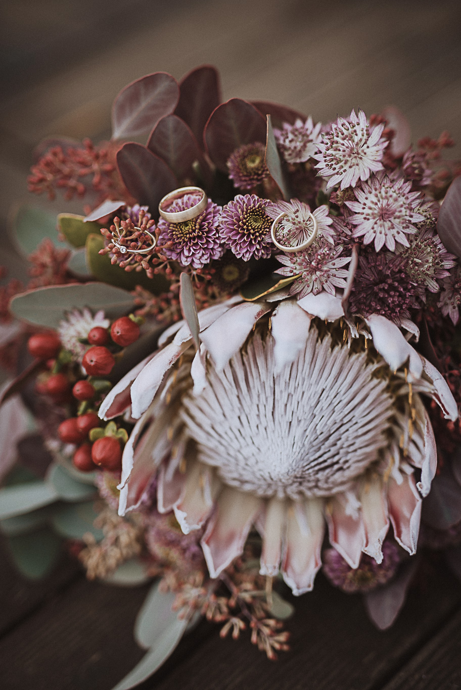 Herbstlicher Brautstrauß mit Protea und roten Beeren auf einem Tisch