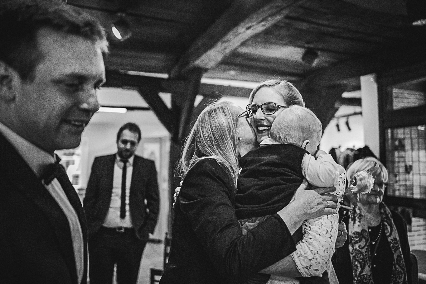 Mann umarmt lachend Frau mit Baby im Arm, Schwarzweißaufnahme