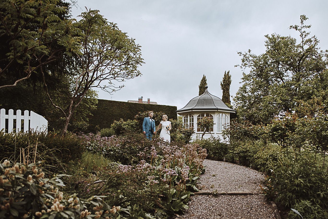 Brautpaar geht auf Kiesweg zu einem Pavillon im Garten