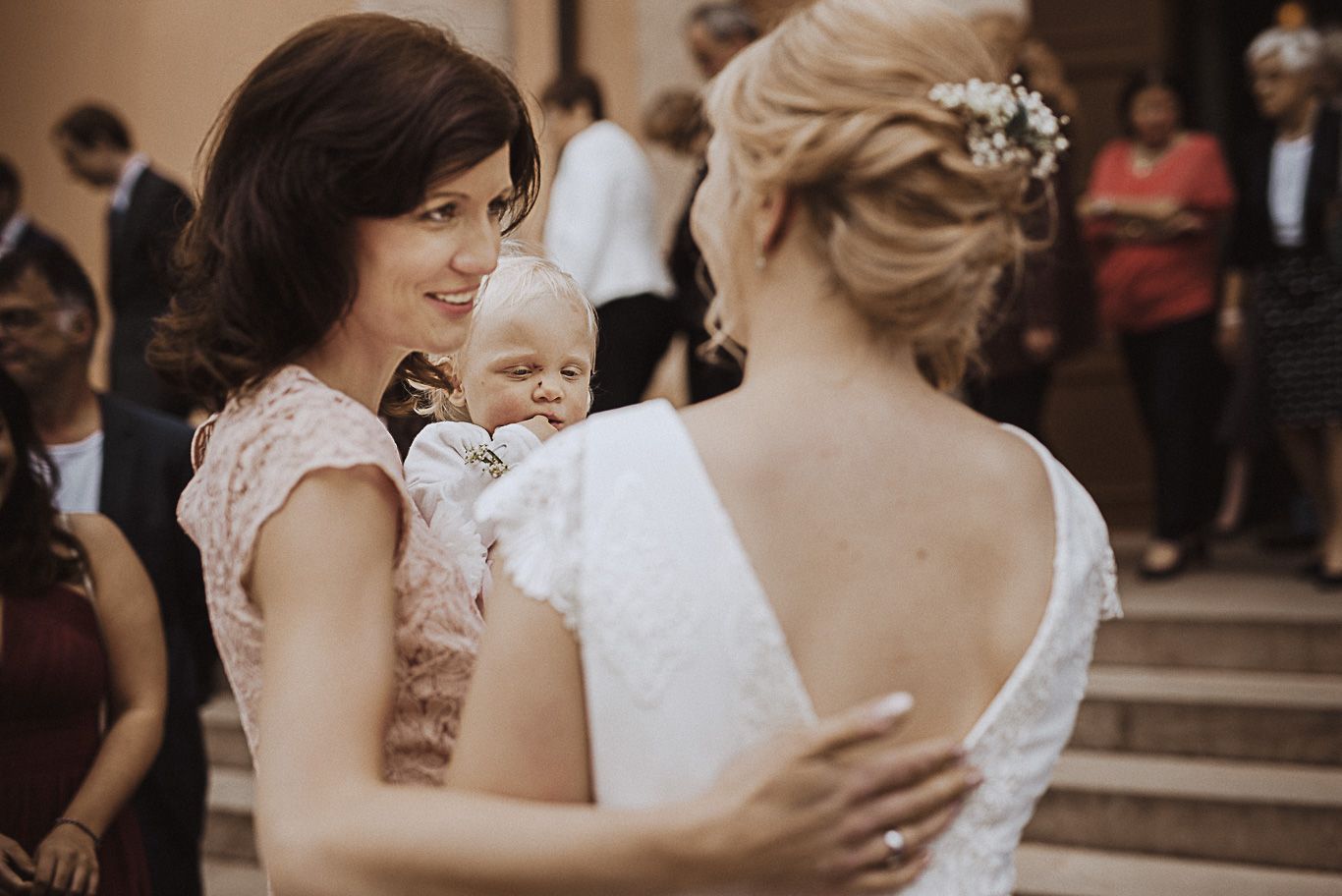 Mutter mit Baby auf dem Arm umarmt die Braut