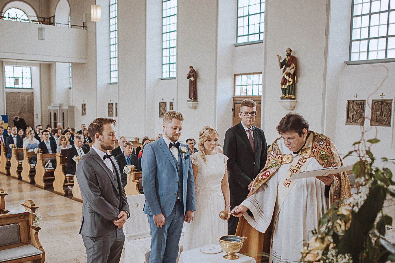 Pfarrer segnet Brautpaar vor Gästen in der Kirche
