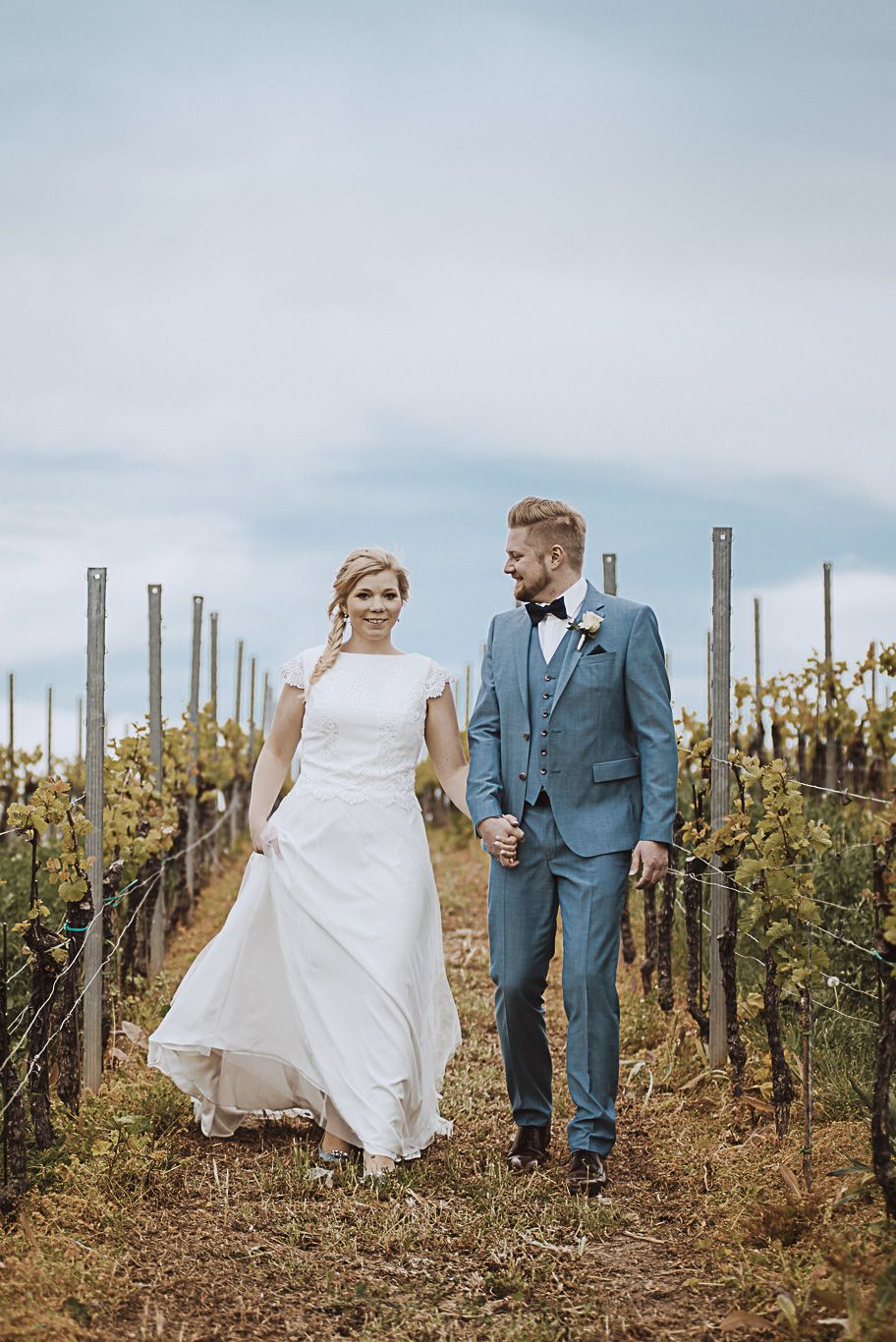 Brautpaar geht Hand in Hand durch die Weinreben im Weingut Fitz-Ritter