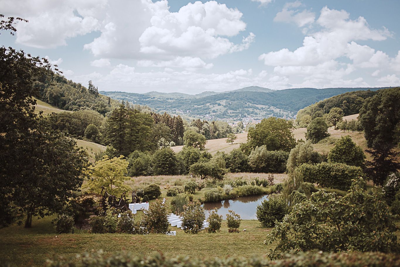 Blick über grüne Hügel und einen Teich in der Landschaft