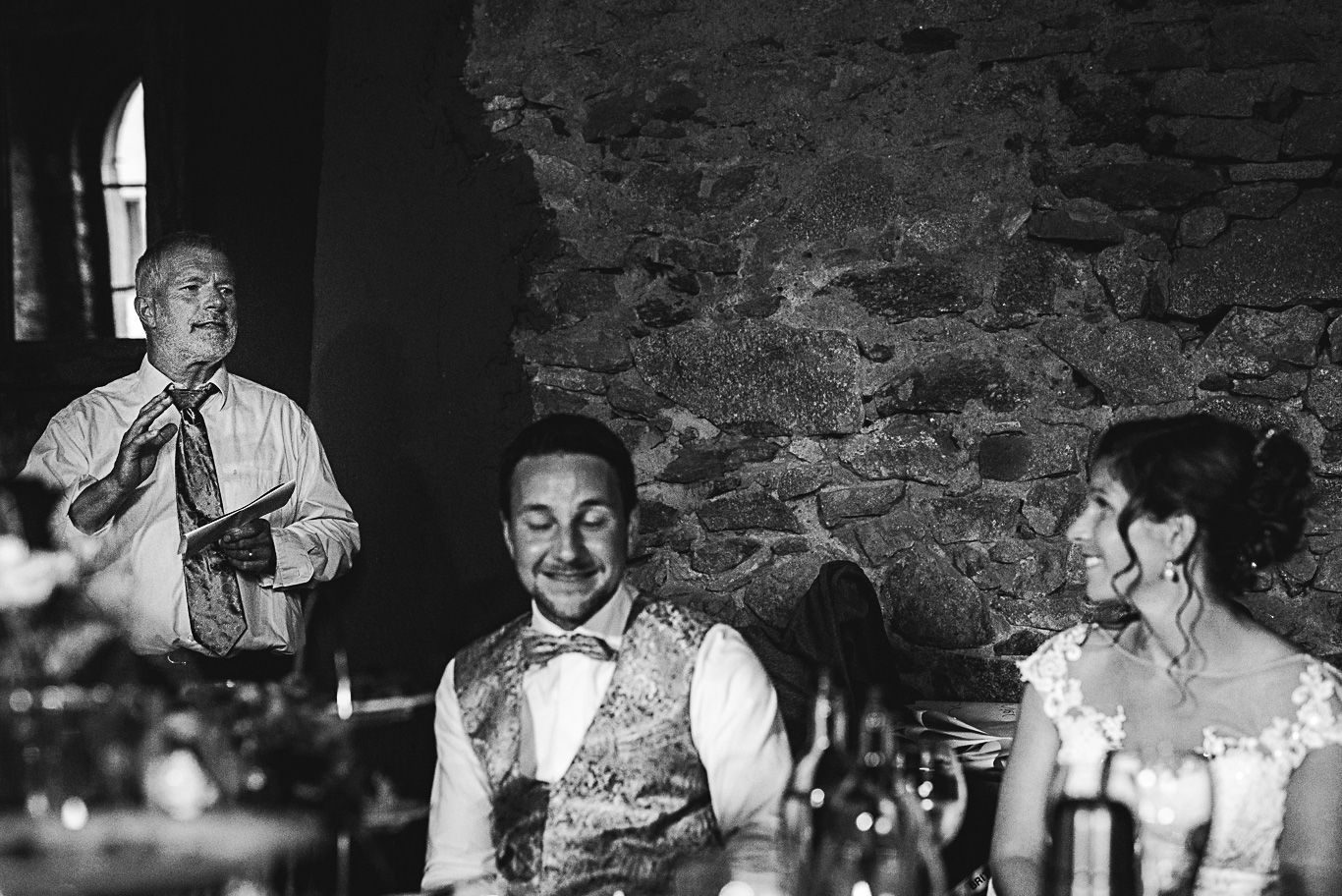 Gast hält Rede zwischen Brautpaar am Tisch, Schwarzweißaufnahme