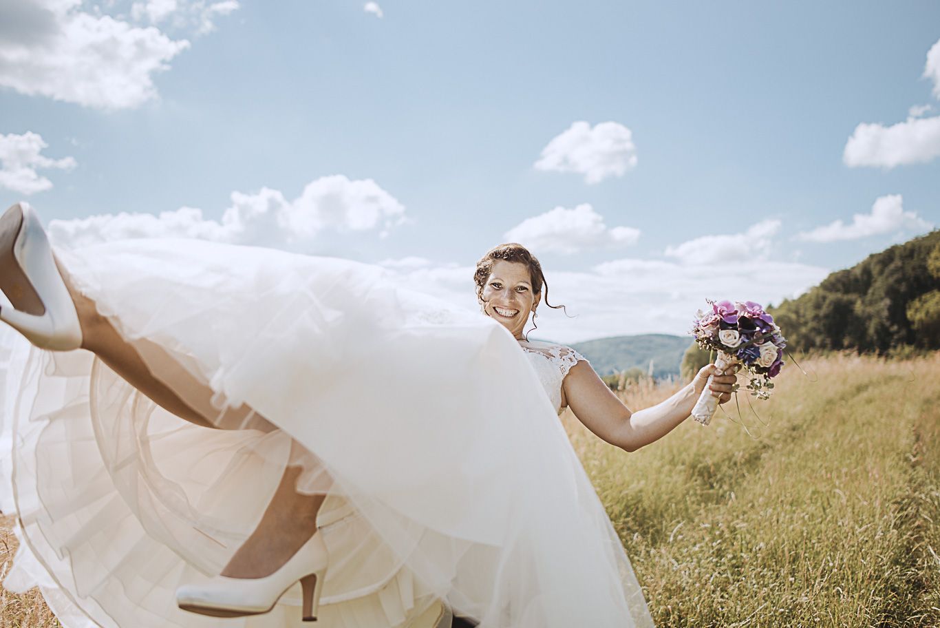Braut schwingt lachend ihr Brautkleid im hohen Gras
