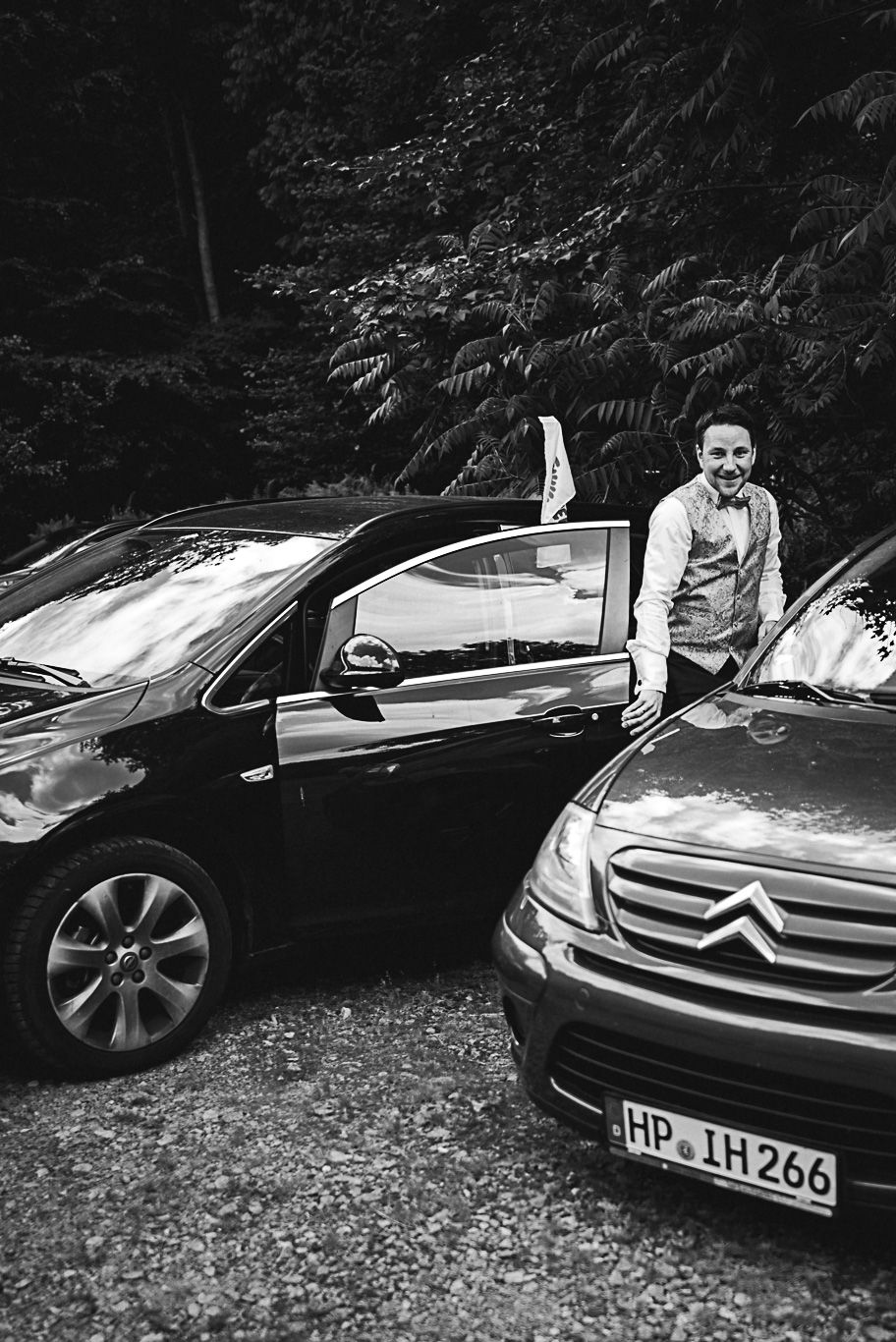 Bräutigam steigt zwischen zwei Autos aus dem Wagen, Schwarzweißaufnahme