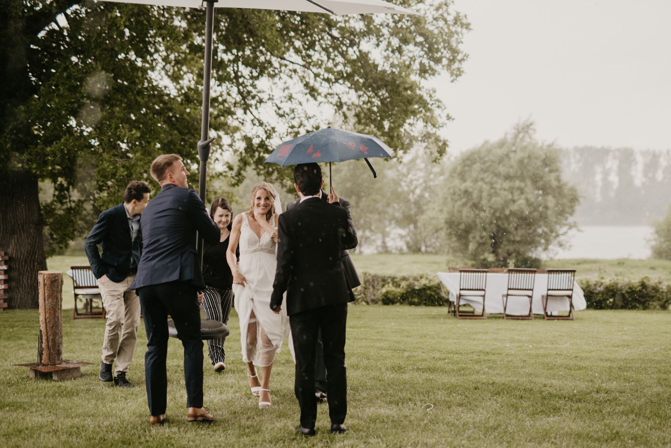 Gäste stehen mit Regenschirm auf regennasser Wiese am Wasser