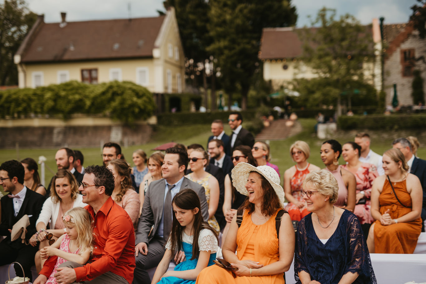 Gäste sitzen in bunten Kleidern bei der Trauung im Freien