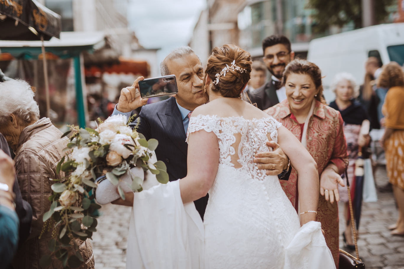 Gäste umarmen Braut und fotografieren mit dem Handy auf dem Marktplatz