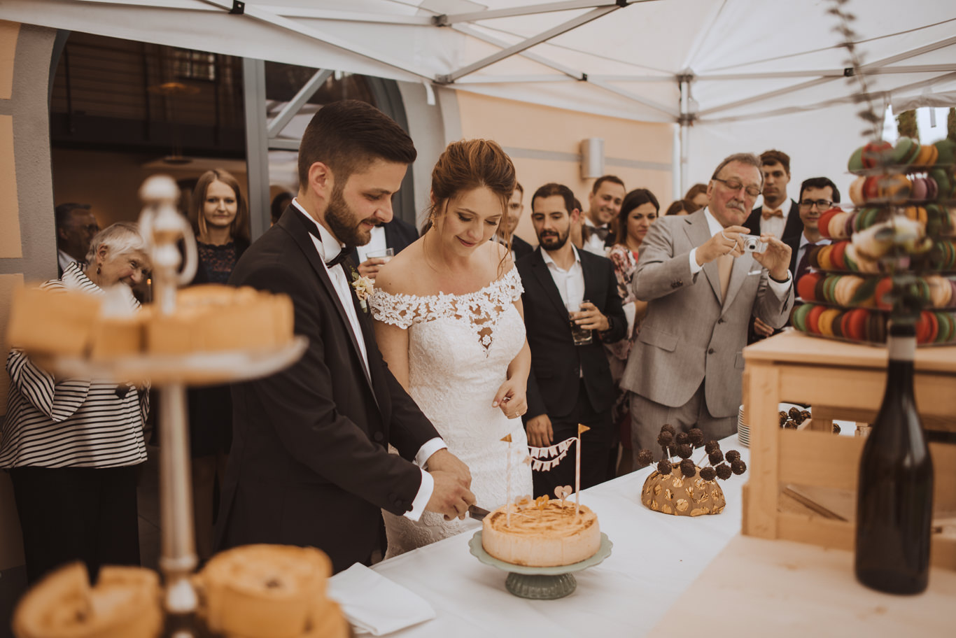 Brautpaar schneidet gemeinsam die Hochzeitstorte vor Gästen an