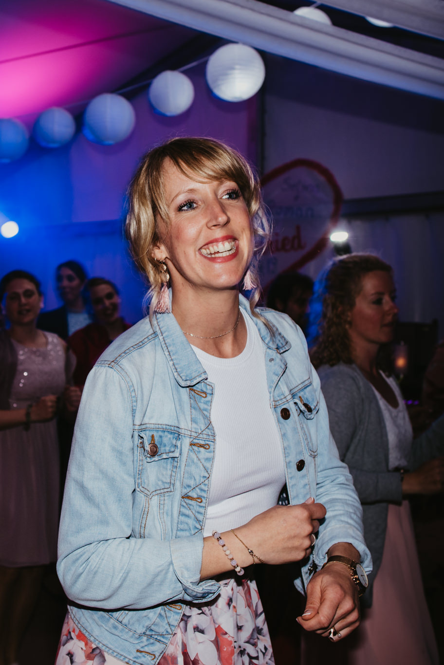 Gästin tanzt lächelnd unter bunten Lichtern in Jeansjacke