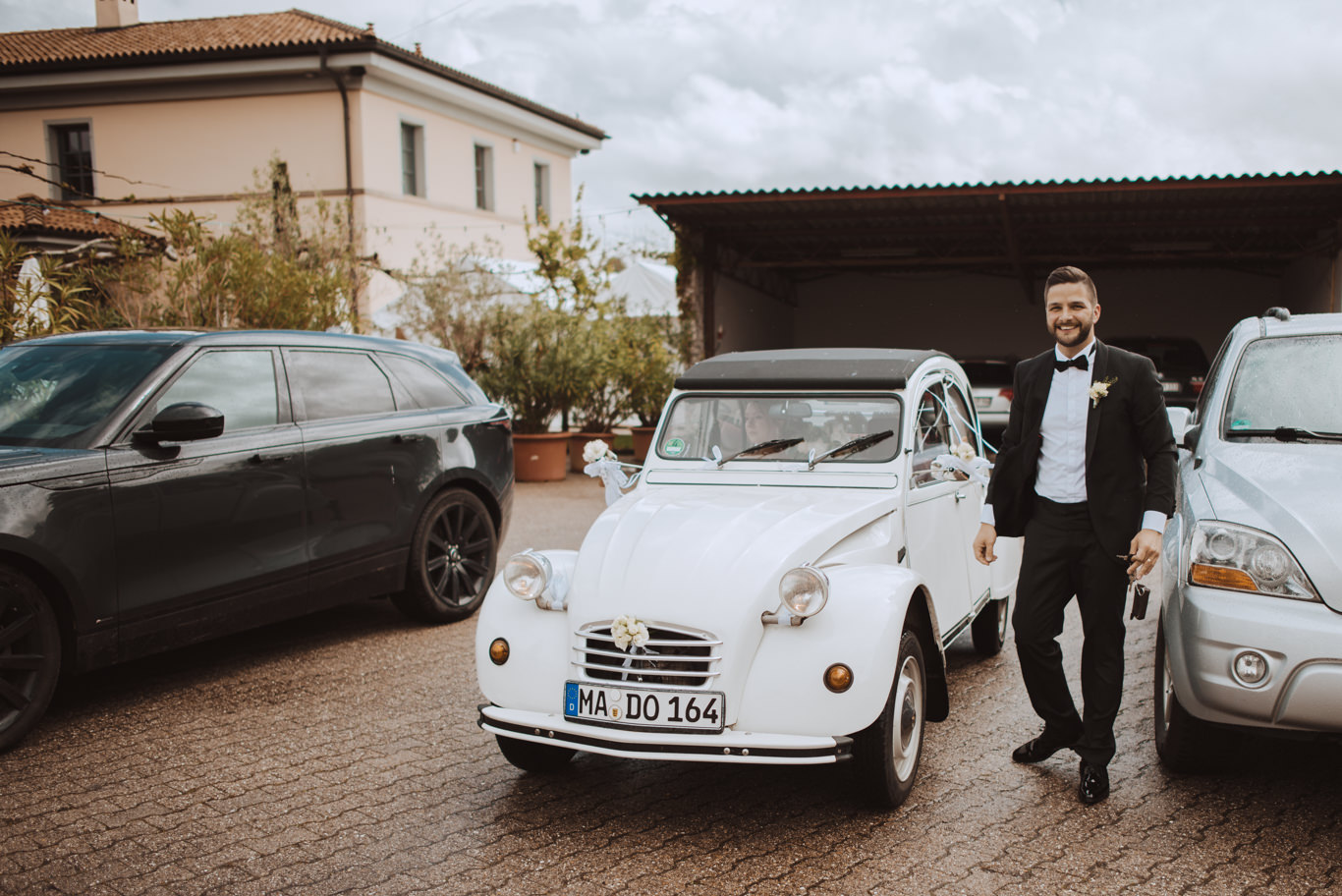 Weißer Oldtimer steht bereit, Bräutigam wartet in der Nähe