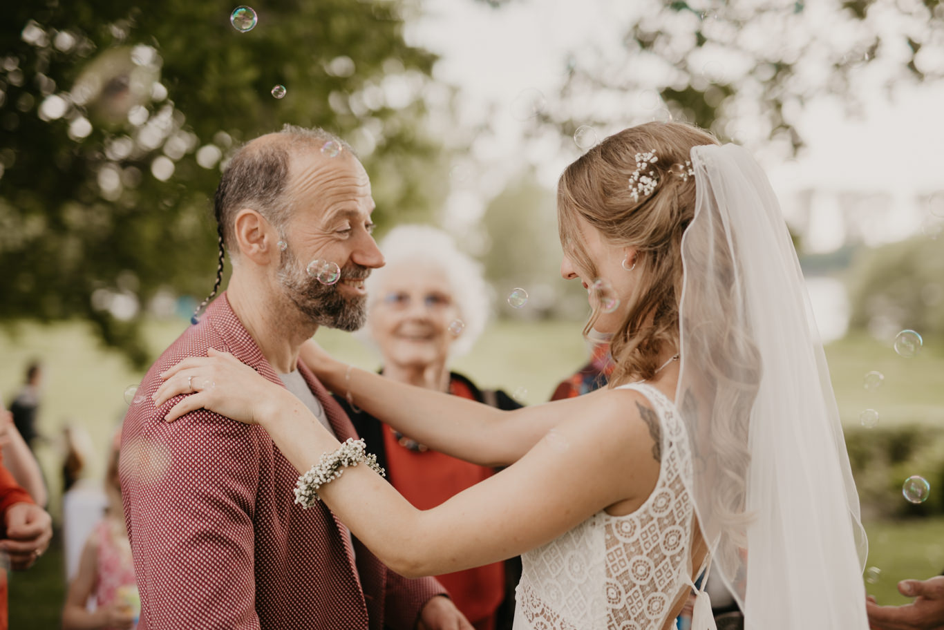 Vater steckt Braut die Ansteckblume an, Seifenblasen im Hintergrund