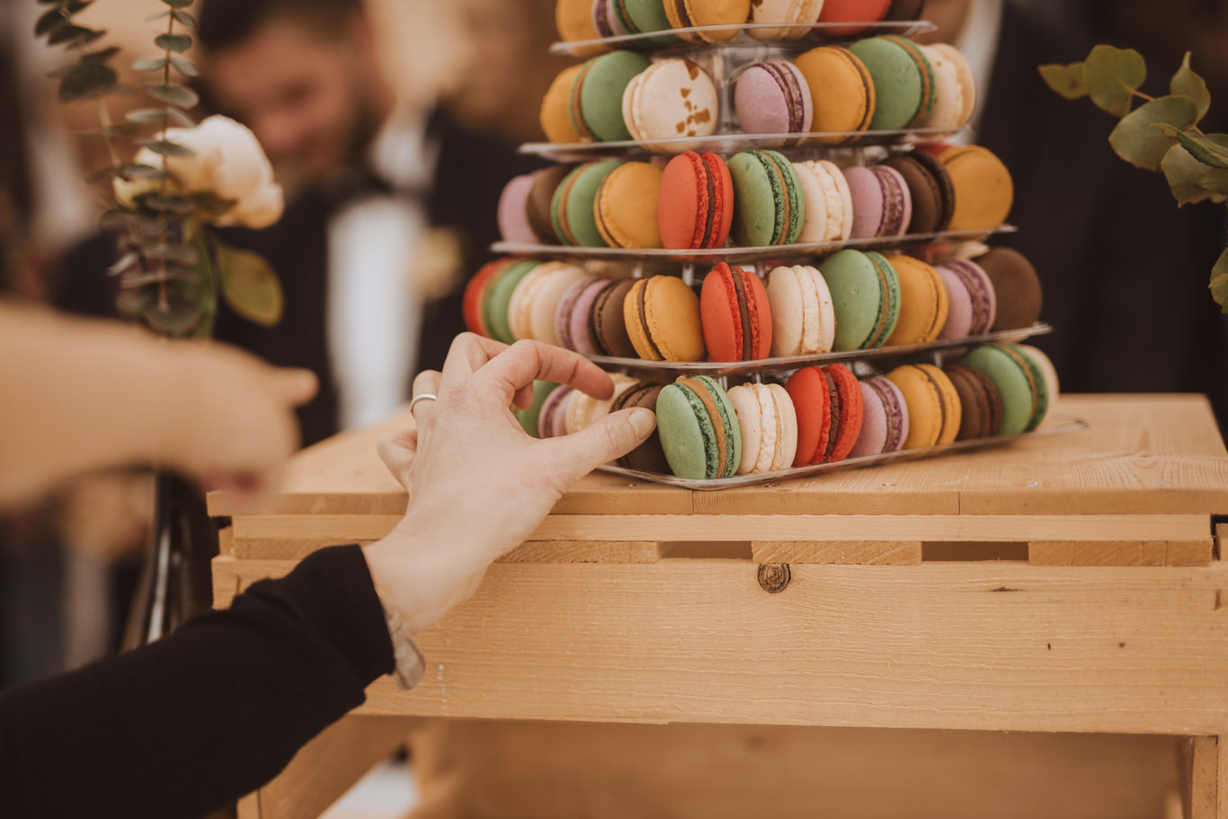 Hand nimmt bunte Macarons von einem hölzernen Ständer