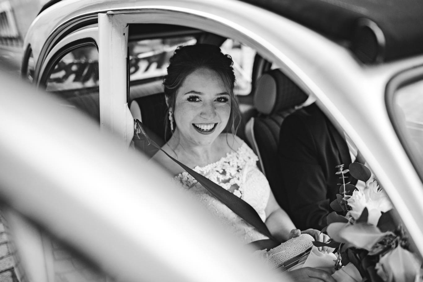 Schwarzweißaufnahme der lächelnden Braut im Oldtimer