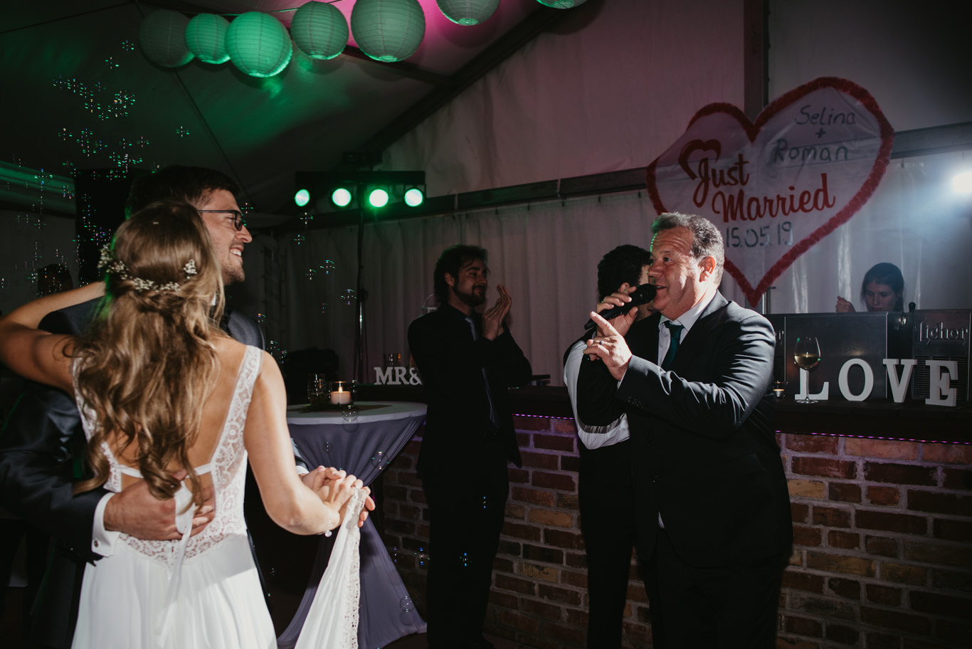 Braut tanzt vor dem Schriftzug „Just Married” mit Gästen