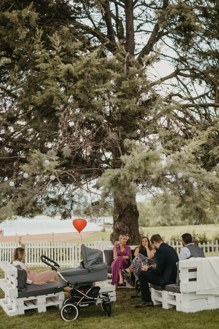 Gäste sitzen unter einem großen Baum mit rotem Herzballon im Hofgut Langenau