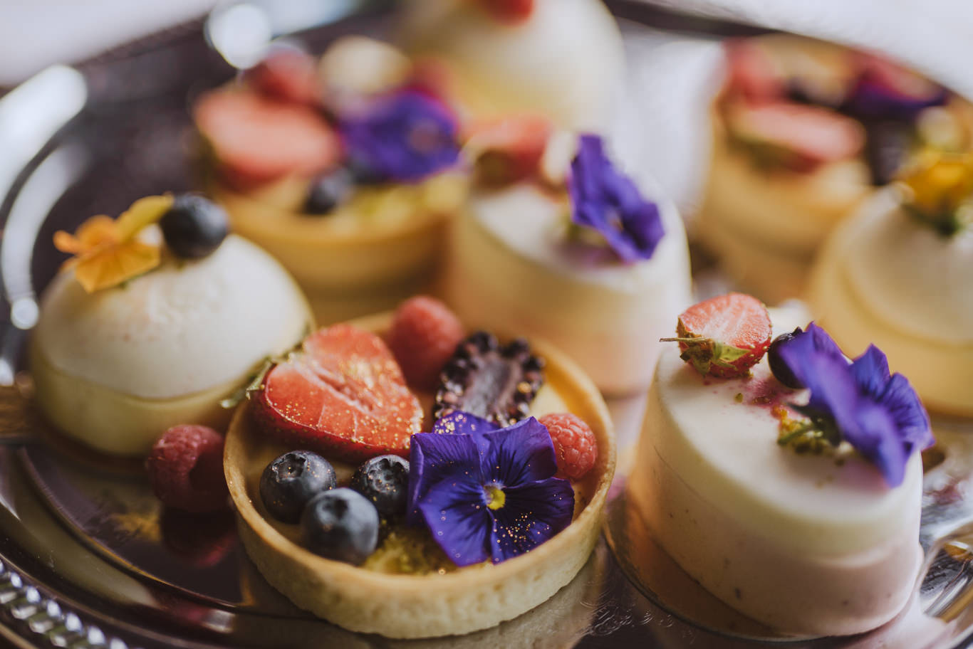Kleine Desserttörtchen mit Beeren und essbaren Blüten dekoriert