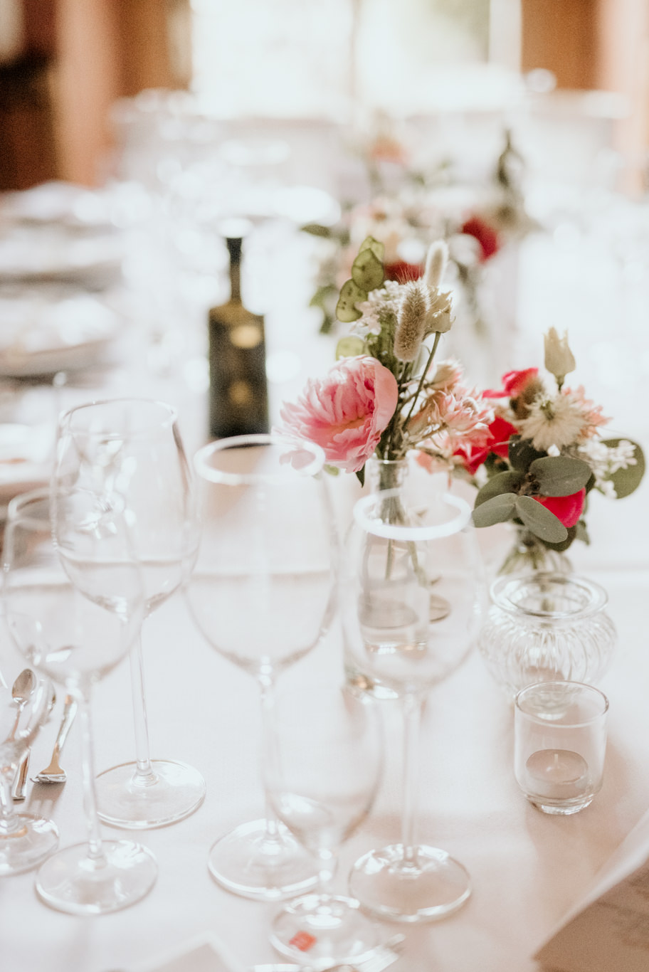 Tischdeko mit rosa Blumen und Weinflasche auf gedecktem Tisch