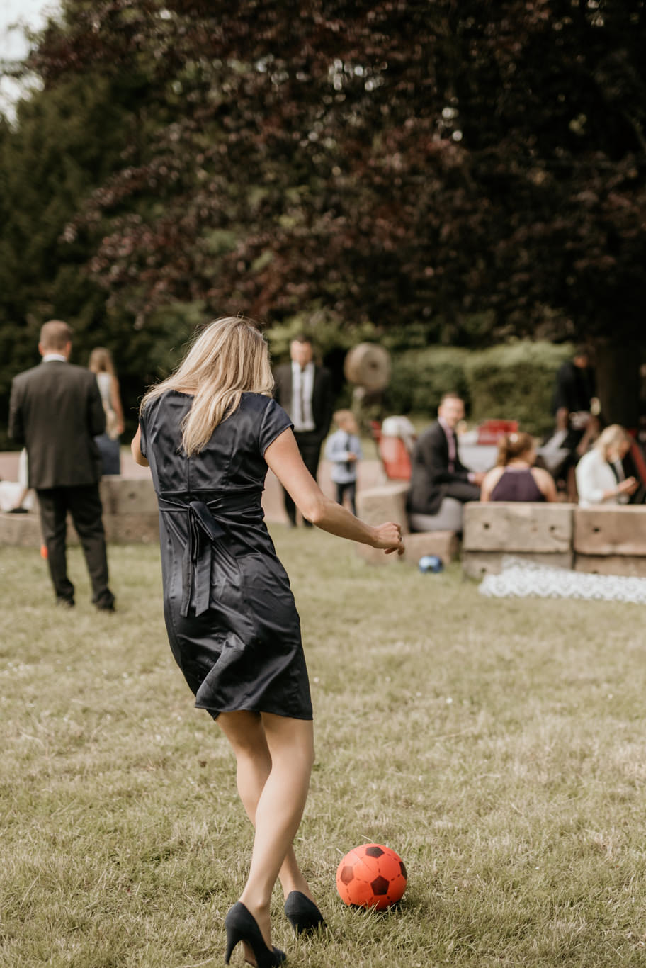 Frau spielt lachend Fußball mit Kindern auf der Wiese