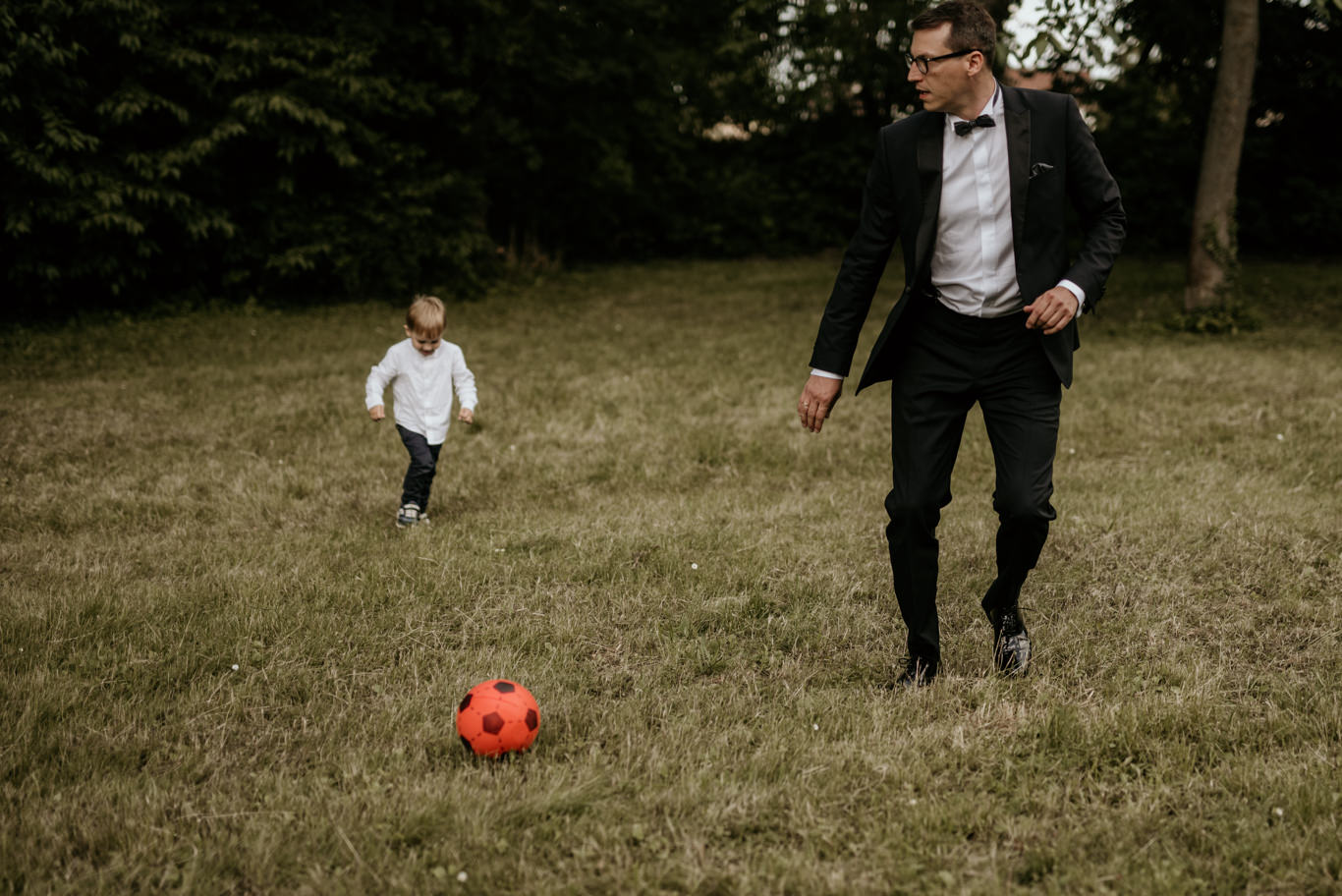 Bräutigam spielt mit kleinem Jungen Fußball auf der Wiese