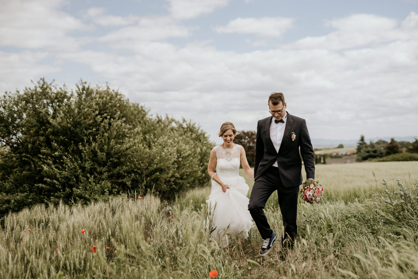 Brautpaar geht Hand in Hand durch ein Feld mit Mohnblumen